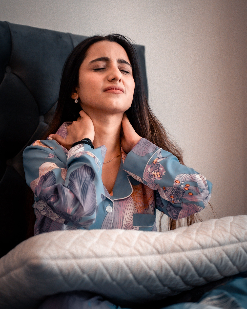 Woman in pajamas with neck pain, lying on a bed.